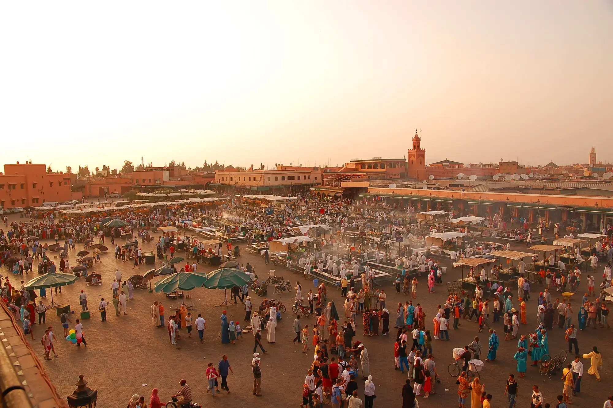 La place Jemaa el-Fna au couchant, foule et étals, minaret de la Koutoubia au loin